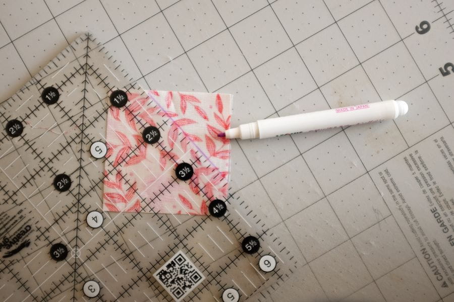 example of quick corner unit with piece of square fabric on quilting mat, with a marker and quilting ruler